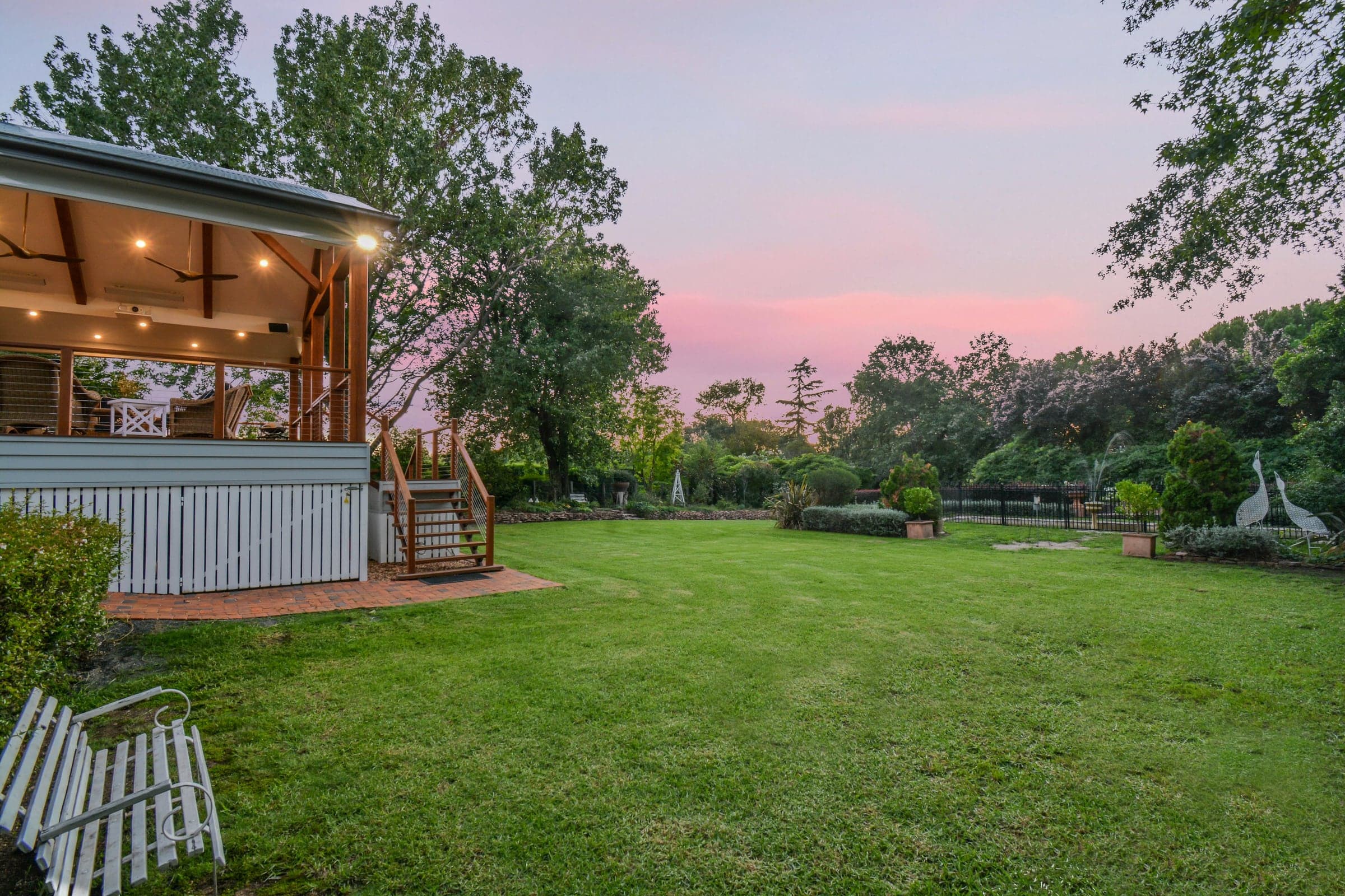 Covered outdoor deck with timber frame and pendant lights overlooking the lawn and garden at sunset, Wahroonga