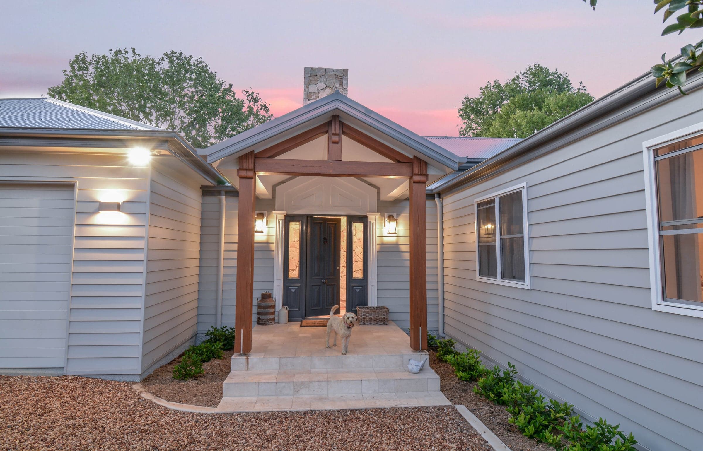 Wahroonga entry portico at dusk with timber posts, lantern wall lights, double door and golden labradoodle on the step