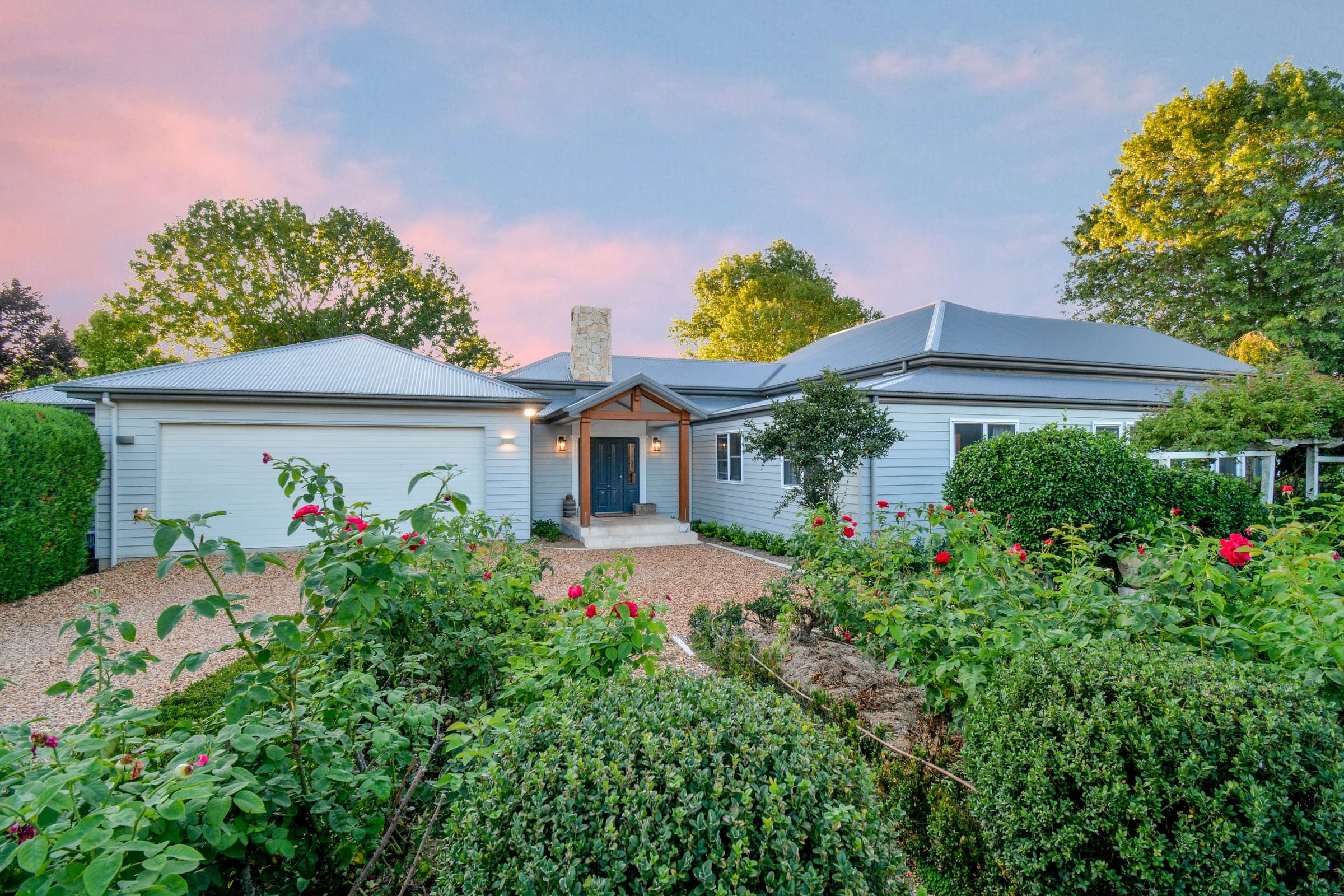 Wahroonga — grey weatherboard home with timber entry portico and rose garden at dusk