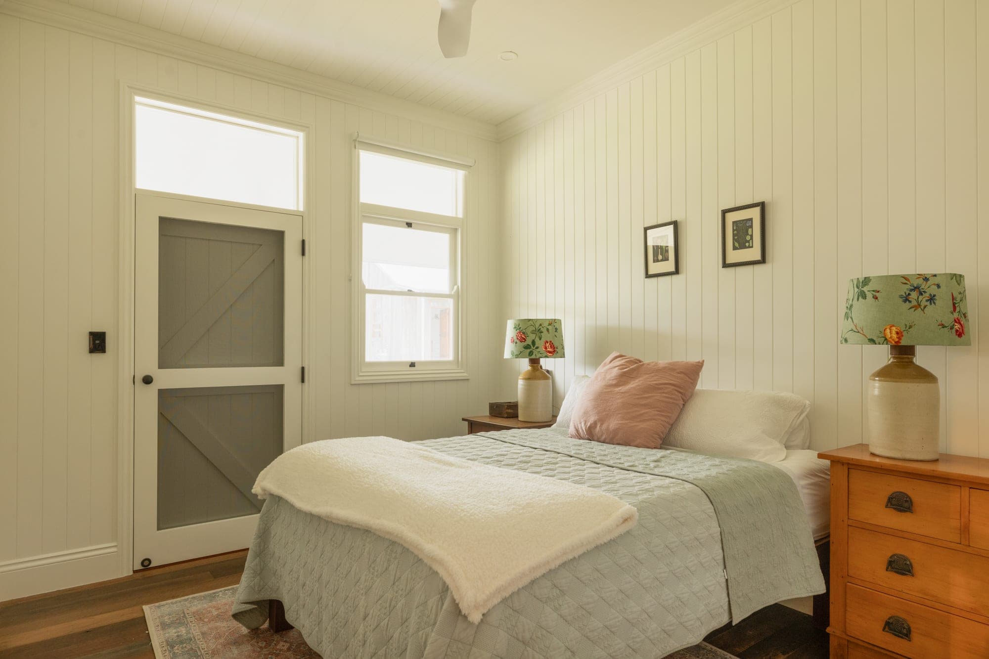 Bedroom with vertical white board-and-batten walls, barn door and natural light from sash windows