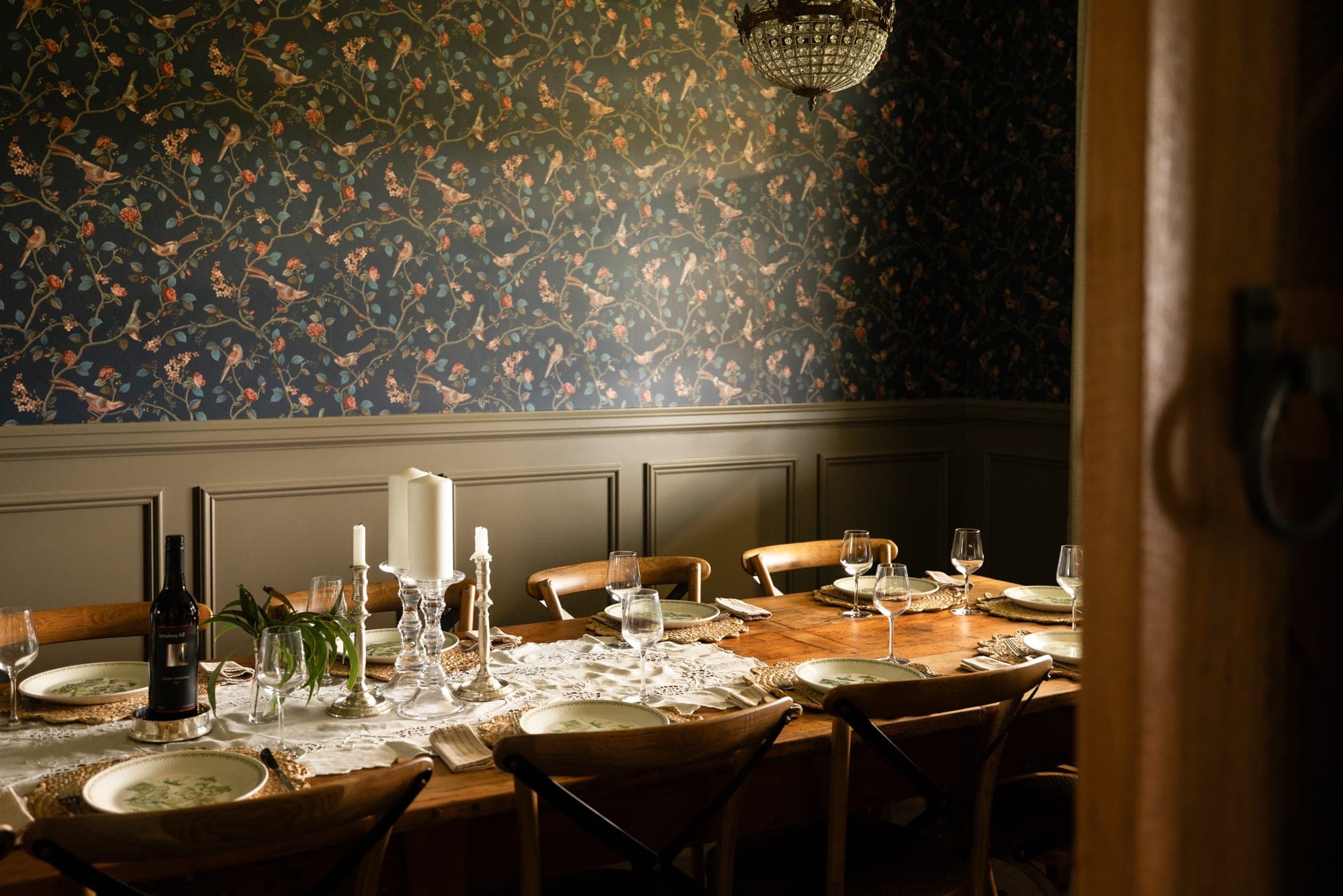 Formal dining room with floor-to-ceiling bird-and-blossom wallpaper, timber table set for eight and crystal chandelier