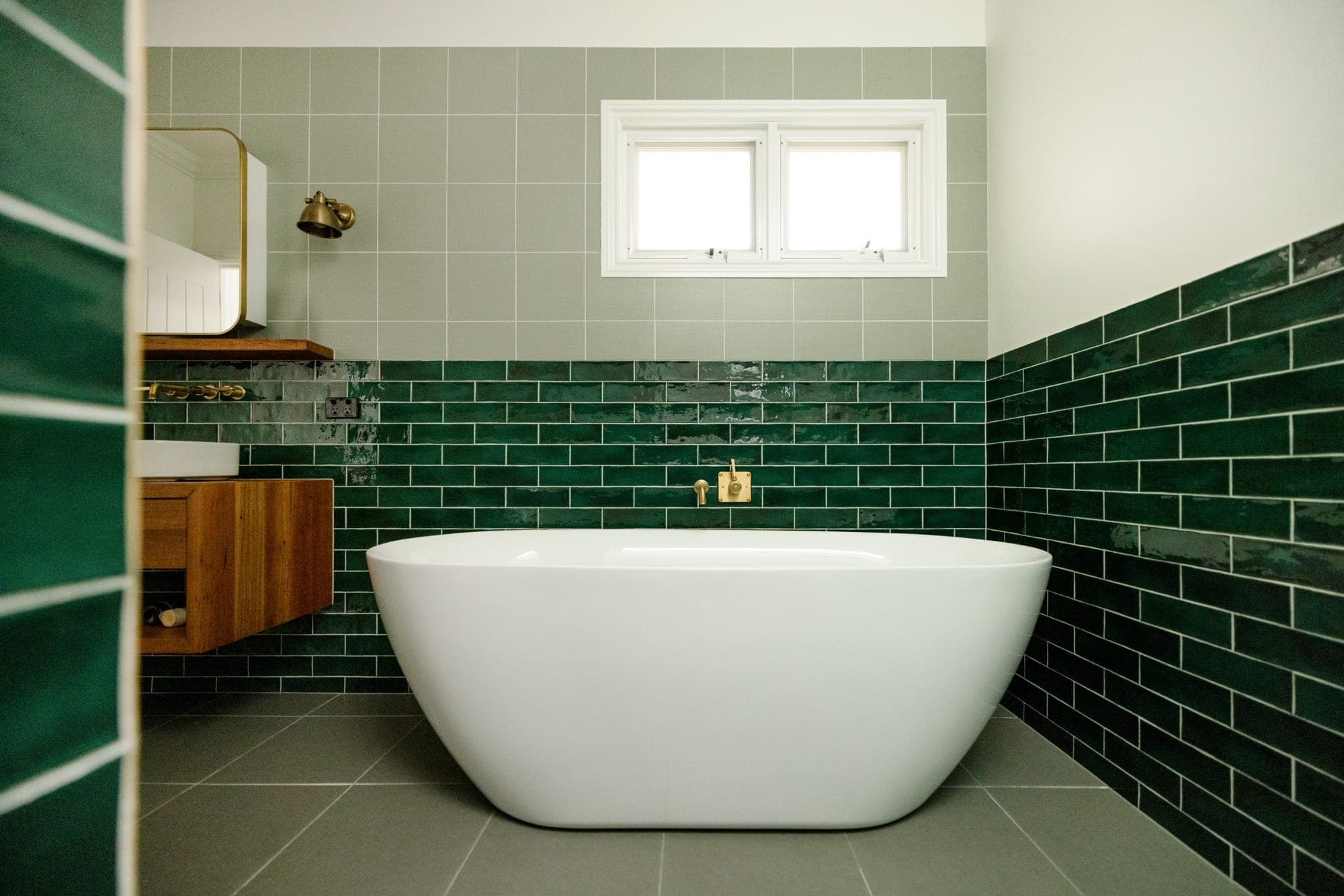 Ensuite with freestanding white bath, hunter green subway tile half-height feature wall and brass fixtures