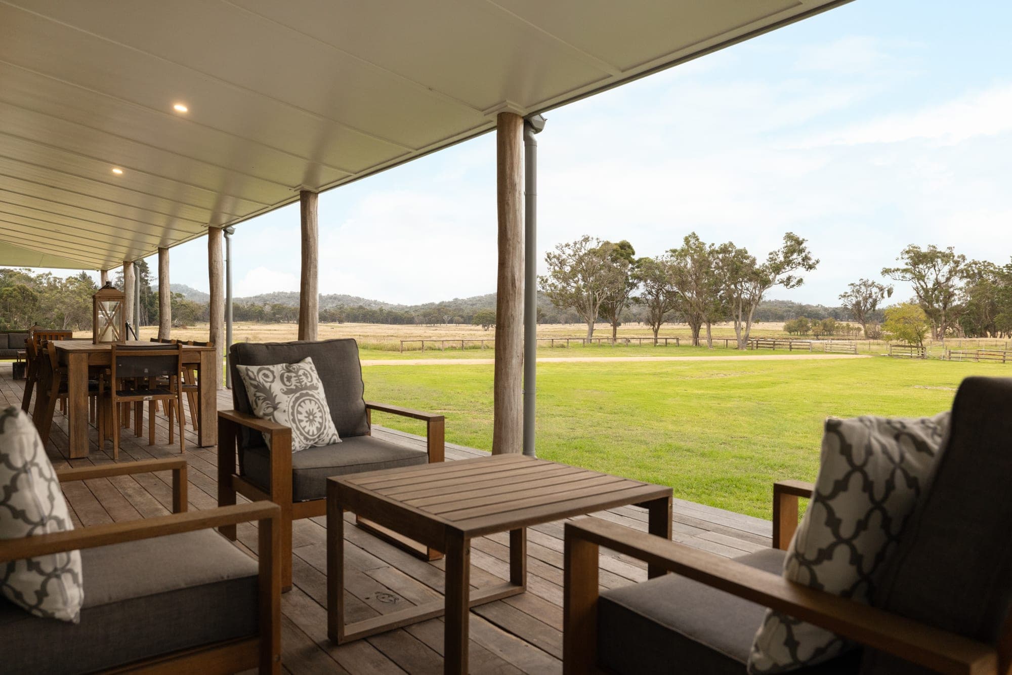 Covered verandah overlooking open paddocks with rough-sawn timber post columns and outdoor lounge seating